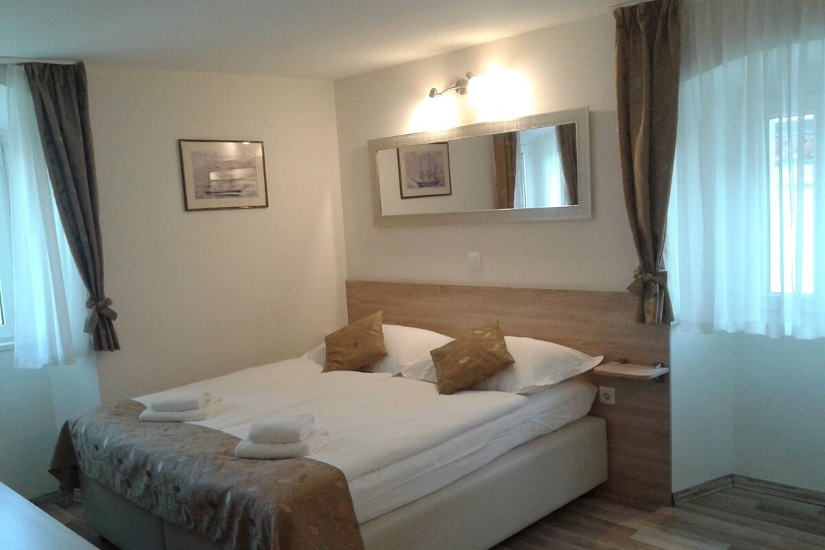 Ein ordentlich bezogenes Bett mit Holz-Kopfteil, einem Nachttisch und einem an der Wand befestigten Spiegel.
