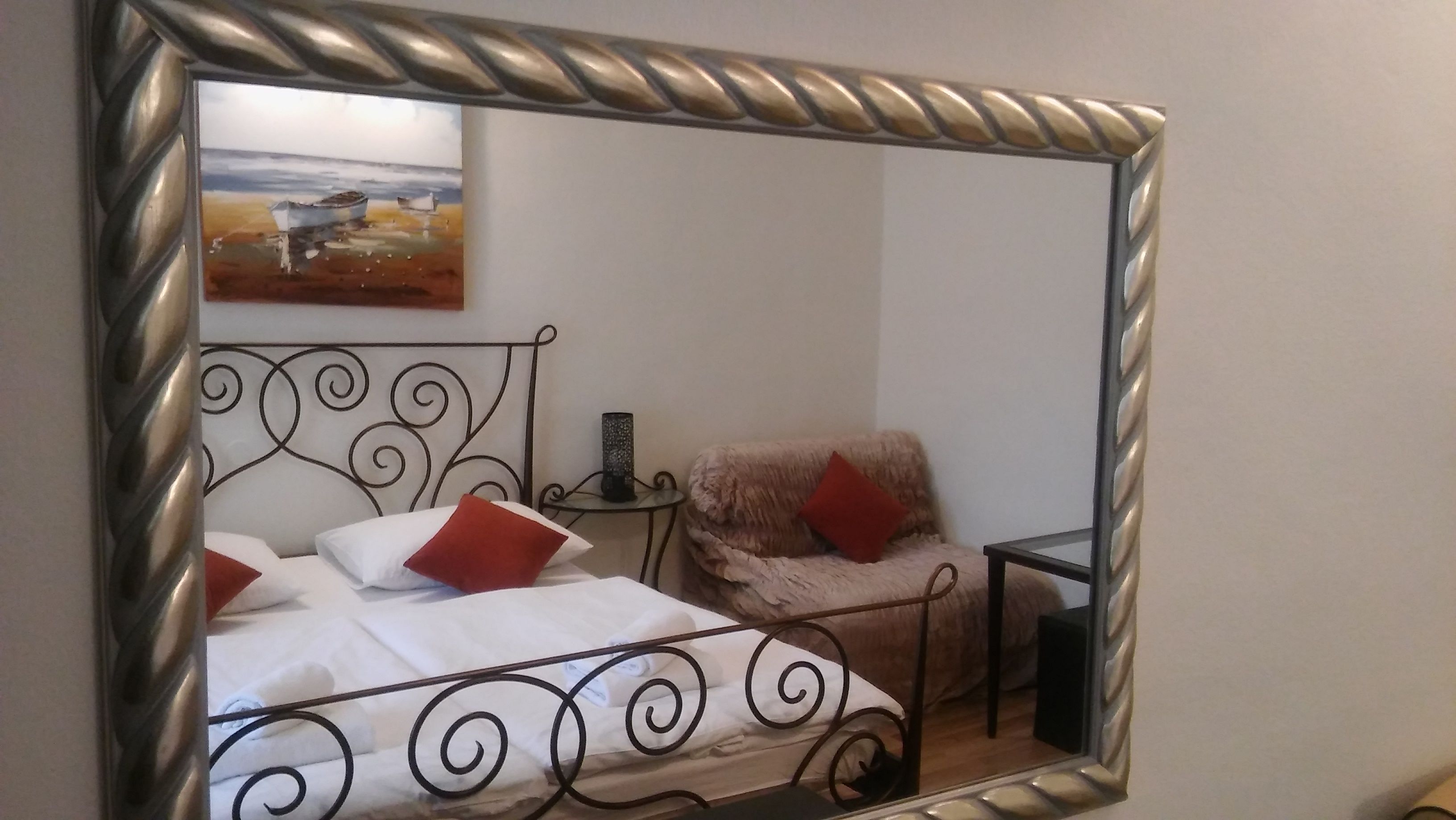 A bedroom with a bed, a chair, a small table, and a painting on the wall.