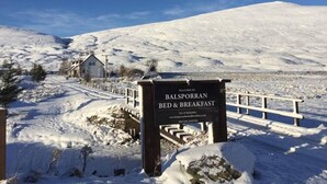 A sign for Balsporran Bed & Breakfast with a snowy landscape in the background. - Balsporran Bed And Breakfast (Dalwhinnie)