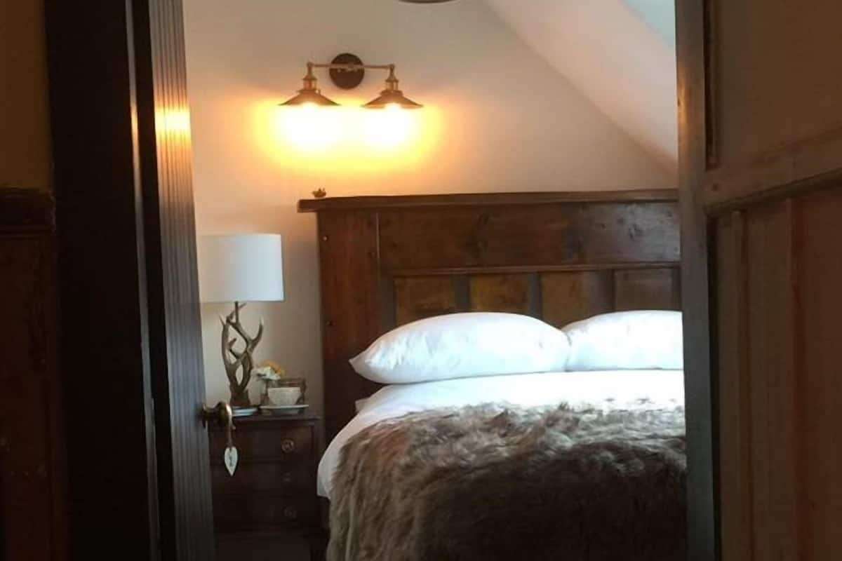 A bedroom with a wooden headboard, a bed with white pillows, a nightstand with a lamp, and a wall-mounted light fixture.