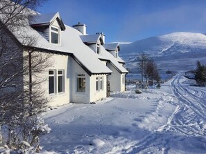 Una casa cubierta de nieve, con cielo despejado y una montaña al fondo.