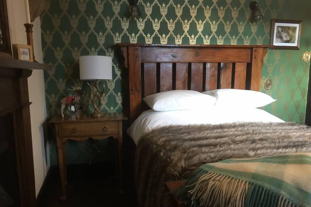 A room with a wooden bed, a nightstand with a lamp, and a patterned wallpaper.