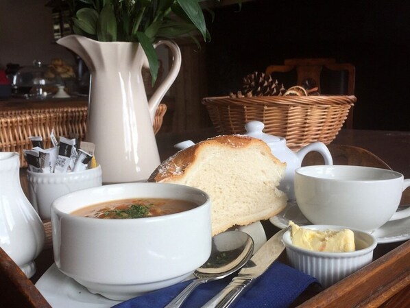Una mesa servida con un tazón de sopa, una rebanada de pan, una jarra y un recipiente pequeño de mantequilla.