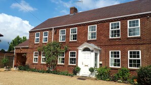 A two-story brick building with a white front door, multiple windows, and a gravel driveway.