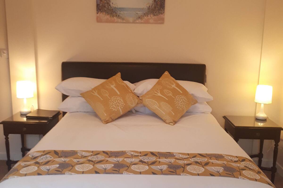 A neatly made bed with a floral-patterned bedspread and two decorative pillows, flanked by two bedside tables with lamps.