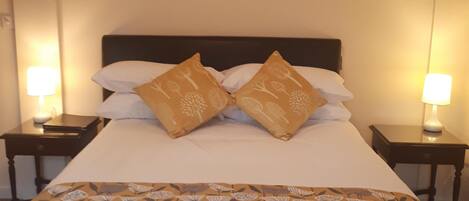 A neatly made bed with a floral-patterned bedspread and two decorative pillows, flanked by two bedside tables with lamps.