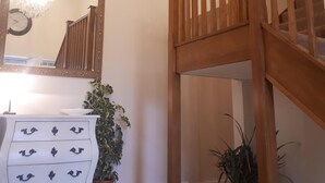 A staircase with wooden railings, a white dresser with decorative handles, a mirror with a gold frame, and potted plants.