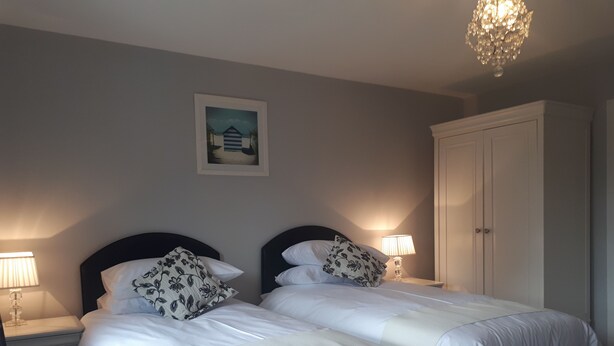 A double bed with white bedding and floral pillows, a nightstand with a lamp, a framed picture on the wall, and a wardrobe.