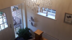 A chandelier hanging from the ceiling, a wooden staircase railing, and a window with a view of the outside.