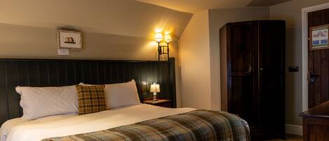 A hotel room with a bed, a nightstand with a lamp, a wardrobe, and a framed fire evacuation plan on the wall.