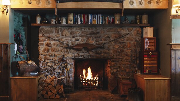 Una chimenea de piedra con fuego, rodeada de estanterías y muebles de madera.