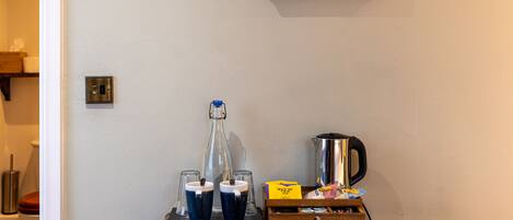 A room with a wooden side table holding a kettle, two mugs, a glass carafe, and a box of tea.