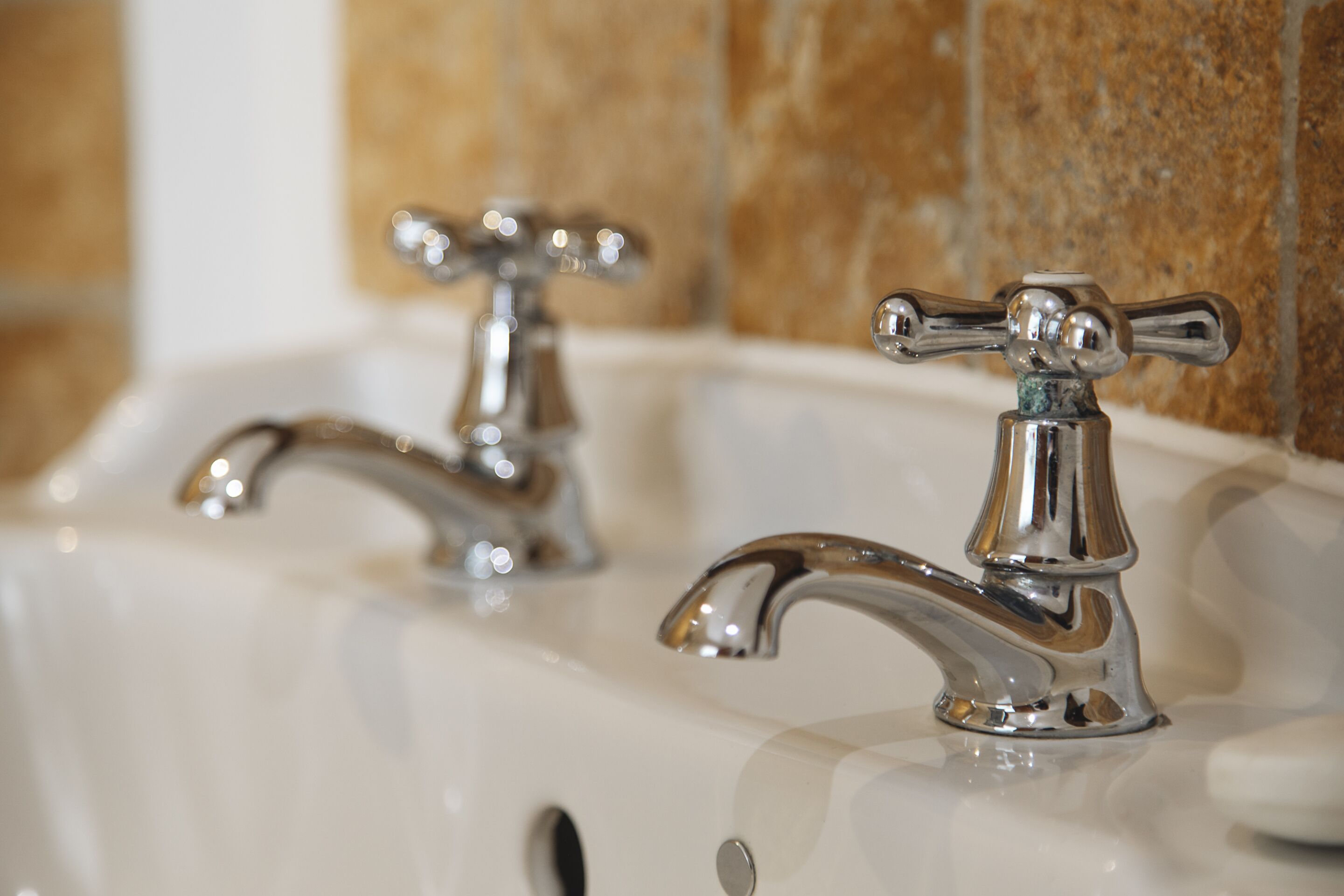 A bathroom sink with two chrome faucets and a marble wall in the background.