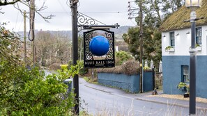 A sign for Blue Ball Inn with a blue sphere, located in a rural setting with a road and greenery. - Blue Ball Inn (Sidmouth)