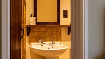 A bathroom with a white sink, two faucets, and a mirror above it. There are two bottles on the shelf above the sink.