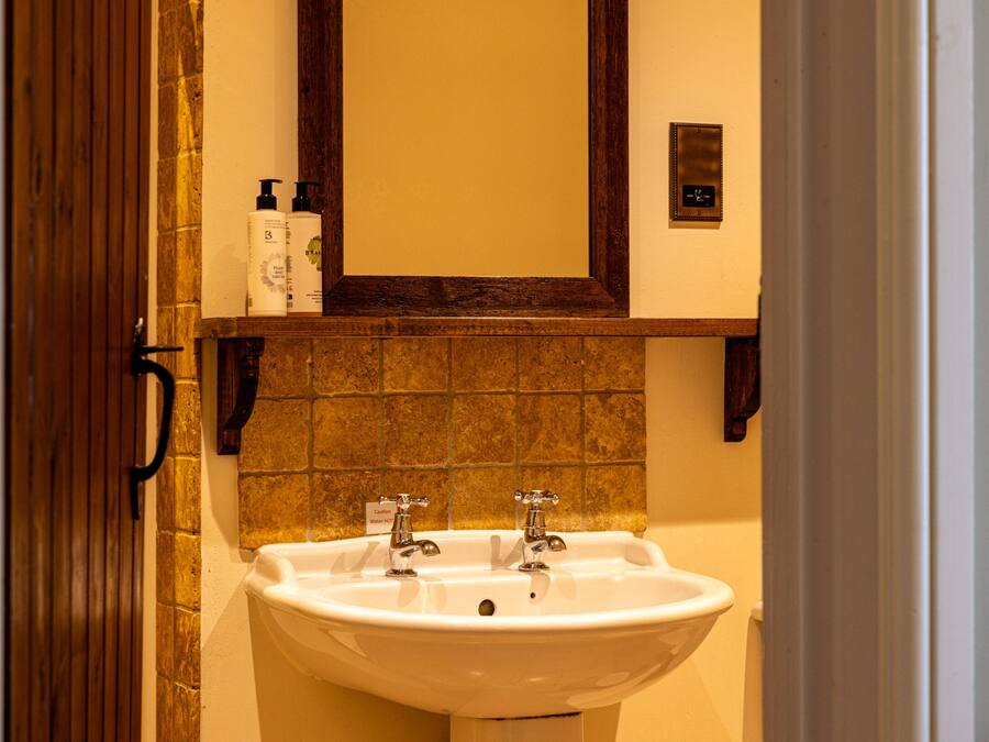 A bathroom with a white sink, two faucets, and a mirror above it. There are two bottles on the shelf above the sink.