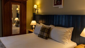 A neatly made bed with white linens and plaid pillows, a wooden wardrobe with a mirror, and two wall-mounted lamps. - Blue Ball Inn (Sidmouth)