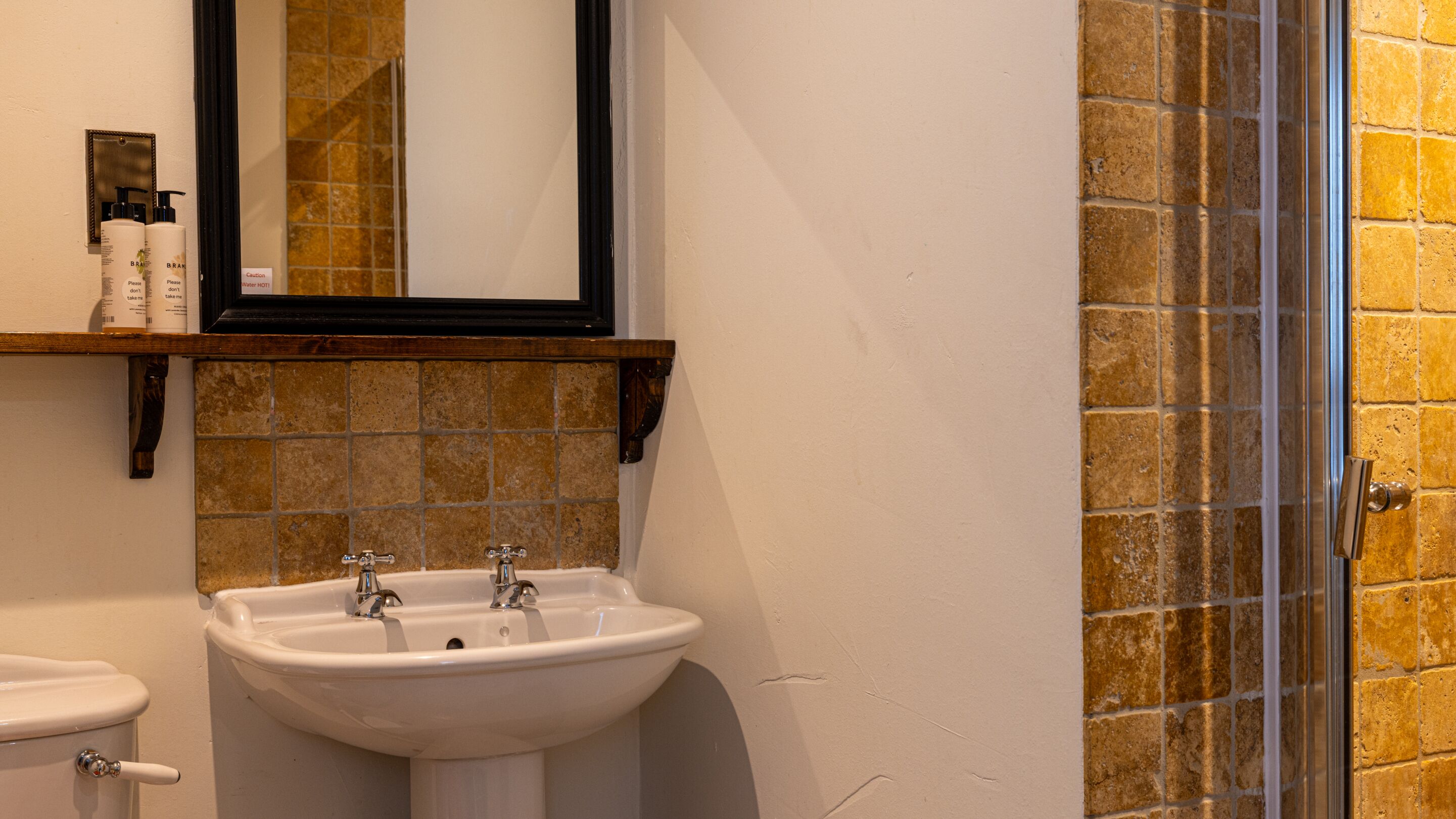 A bathroom with a white sink, a mirror, and a shower with a brick wall.