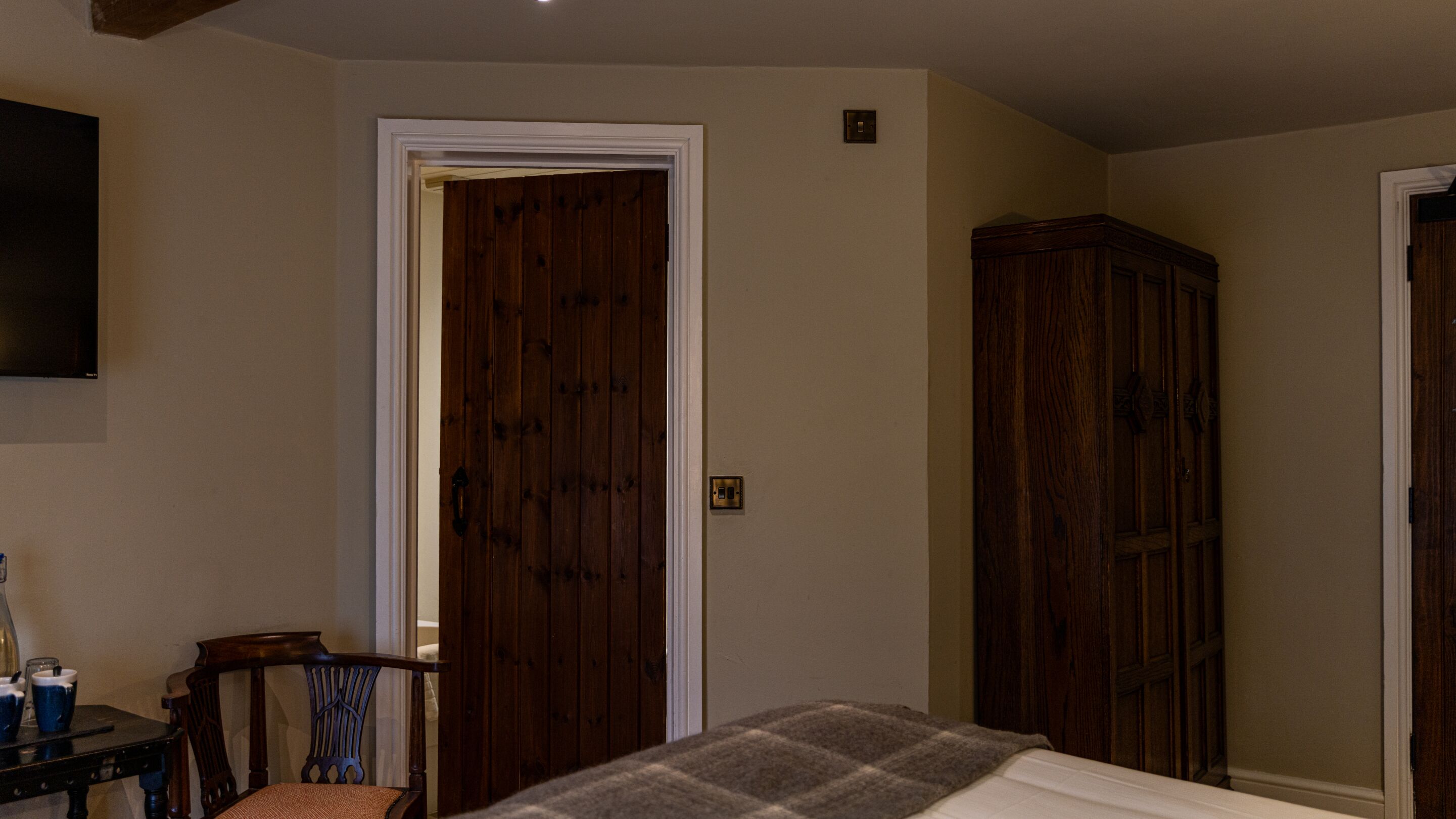 A bedroom with a bed, a wooden wardrobe, a television on the wall, and a door.