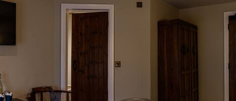 A bedroom with a bed, a wooden wardrobe, a television on the wall, and a door.