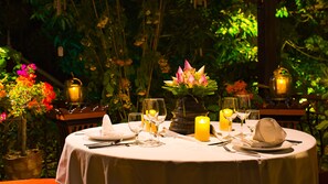 A round table set for a meal with candles, glasses, and a vase of flowers. - Montra Nivesha Residence (Siem Reap)