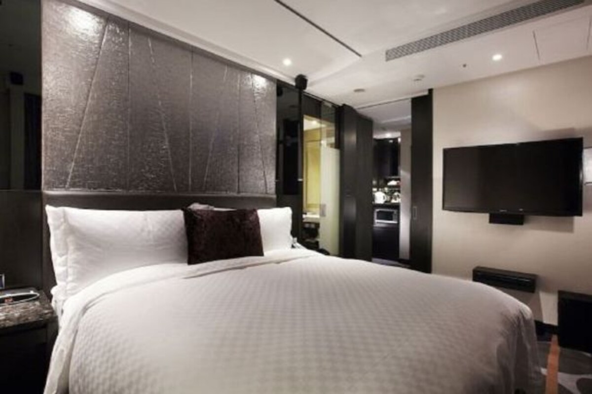 Ett modernt hotellrum med en stor säng, en platt-TV som är monterad på väggen och en mörk sänggavel.