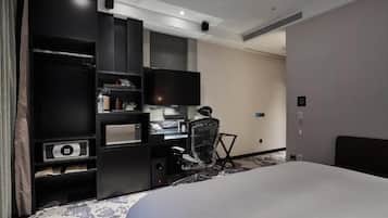 A hotel room with a large bed, a desk with a computer, a chair, a TV, and a wardrobe.