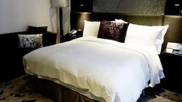 A neatly made bed with a white comforter and two pillows, a bedside lamp, and a nightstand with a phone.
