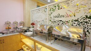 A buffet setup with a decorative backdrop, a wooden cabinet with dishes, and a marble countertop.