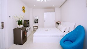 A modern bedroom with a white bed, a blue chair, a dresser, a vanity with a mirror, and a ceiling light fixture.