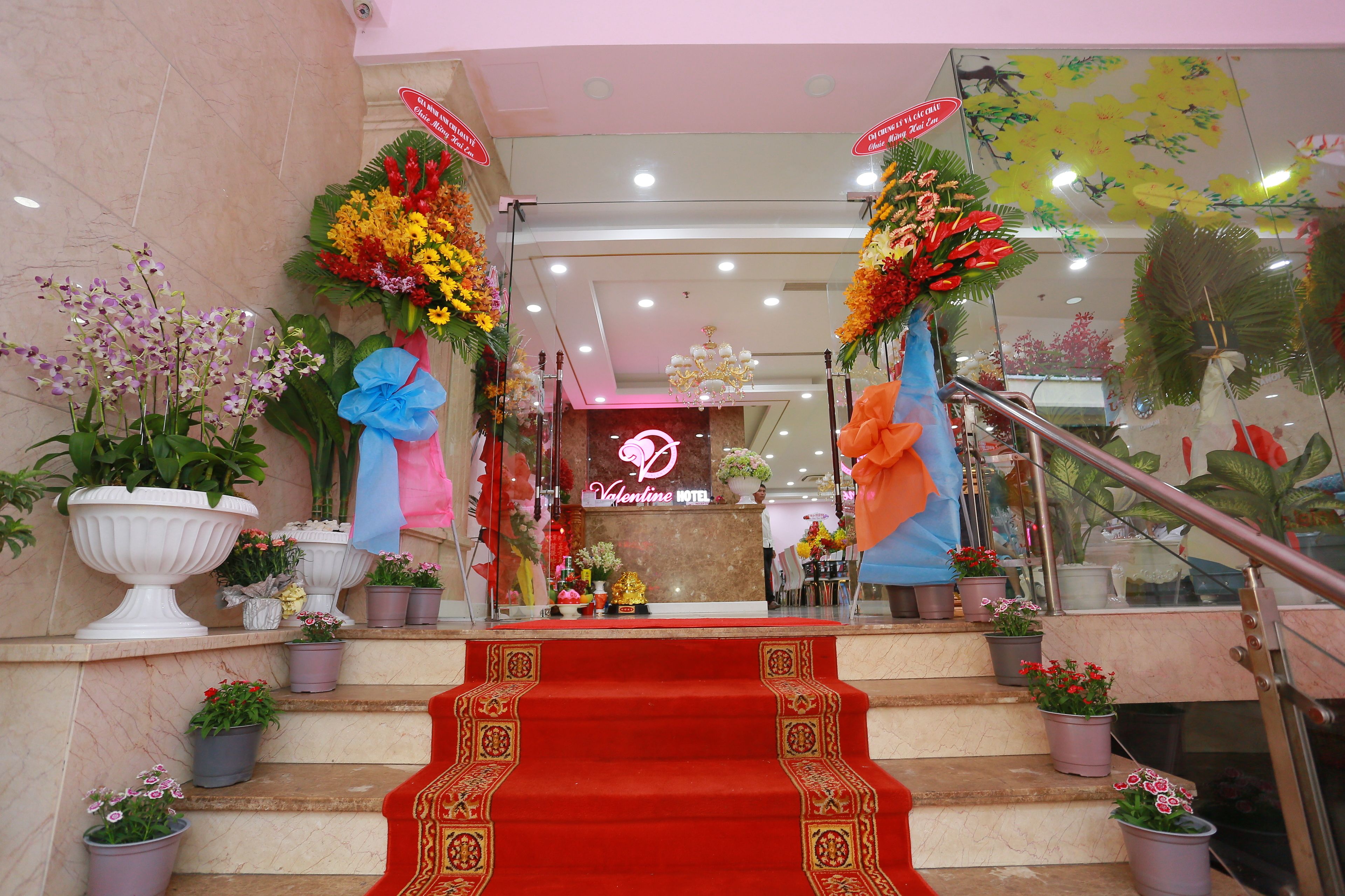 A hotel entrance with a red carpeted staircase, potted plants, and a neon sign.