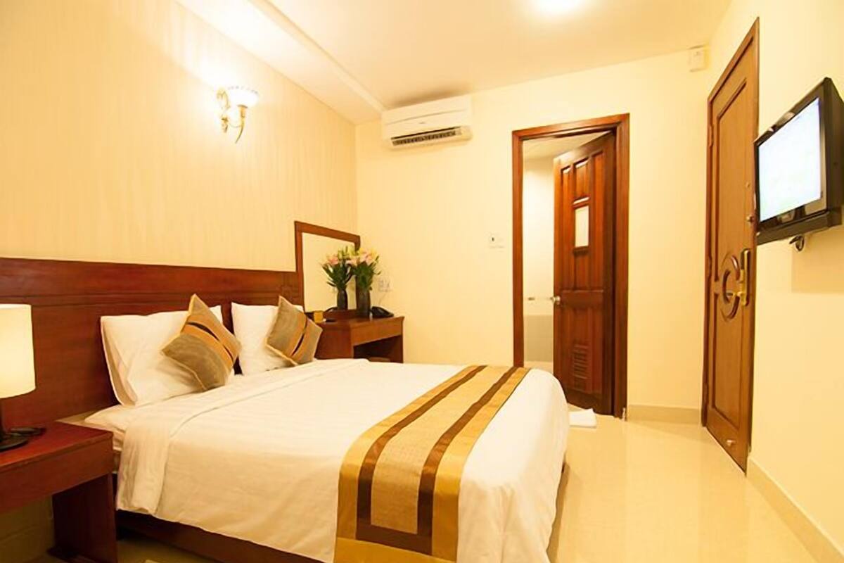 Une chambre d’hôtel avec un grand lit, une table de chevet avec une lampe, un téléviseur fixé au mur et une porte en bois.