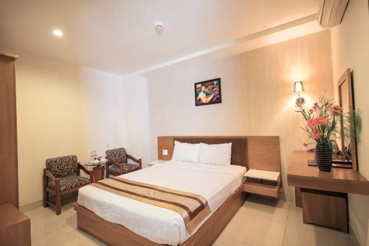Een hotelkamer met een groot bed, twee fauteuils, een nachtkastje en een bijzettafeltje.