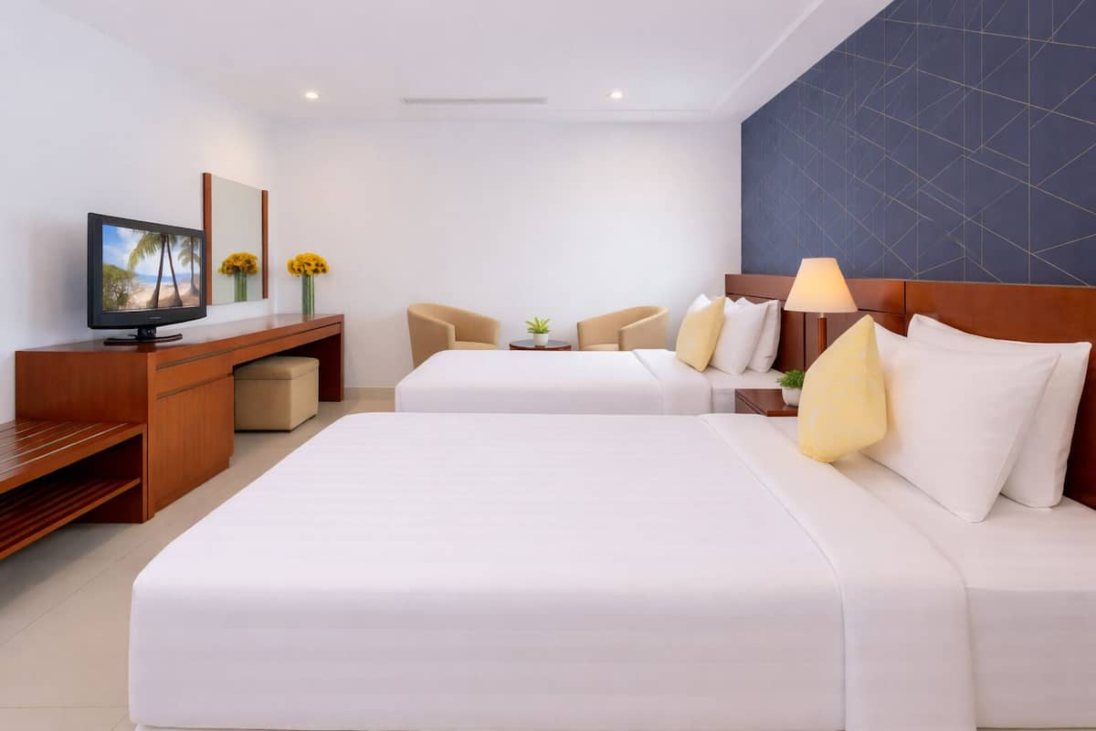 Ein Hotelzimmer mit zwei Betten, einem Schreibtisch, einem Fernseher und einer Sitzecke mit Stühlen und einem kleinen Tisch.