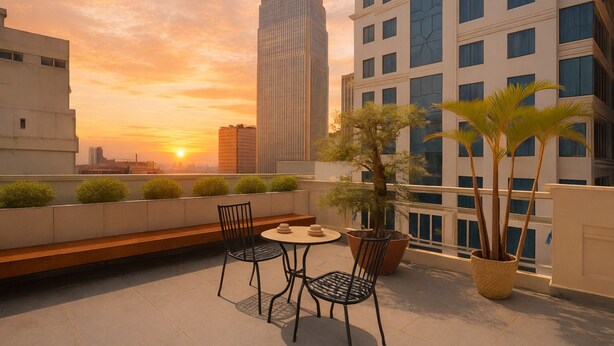 Een dakterras met uitzicht op een zonsondergang, met een tafel en stoelen, plantenbakken en een stadsachtergrond.