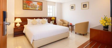 A hotel room with a large bed, a desk, a chair, and a small table with flowers.