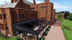 A modern extension with glass walls and outdoor seating, attached to a traditional brick building. - Abbey House Hotel (Barrow-in-Furness)