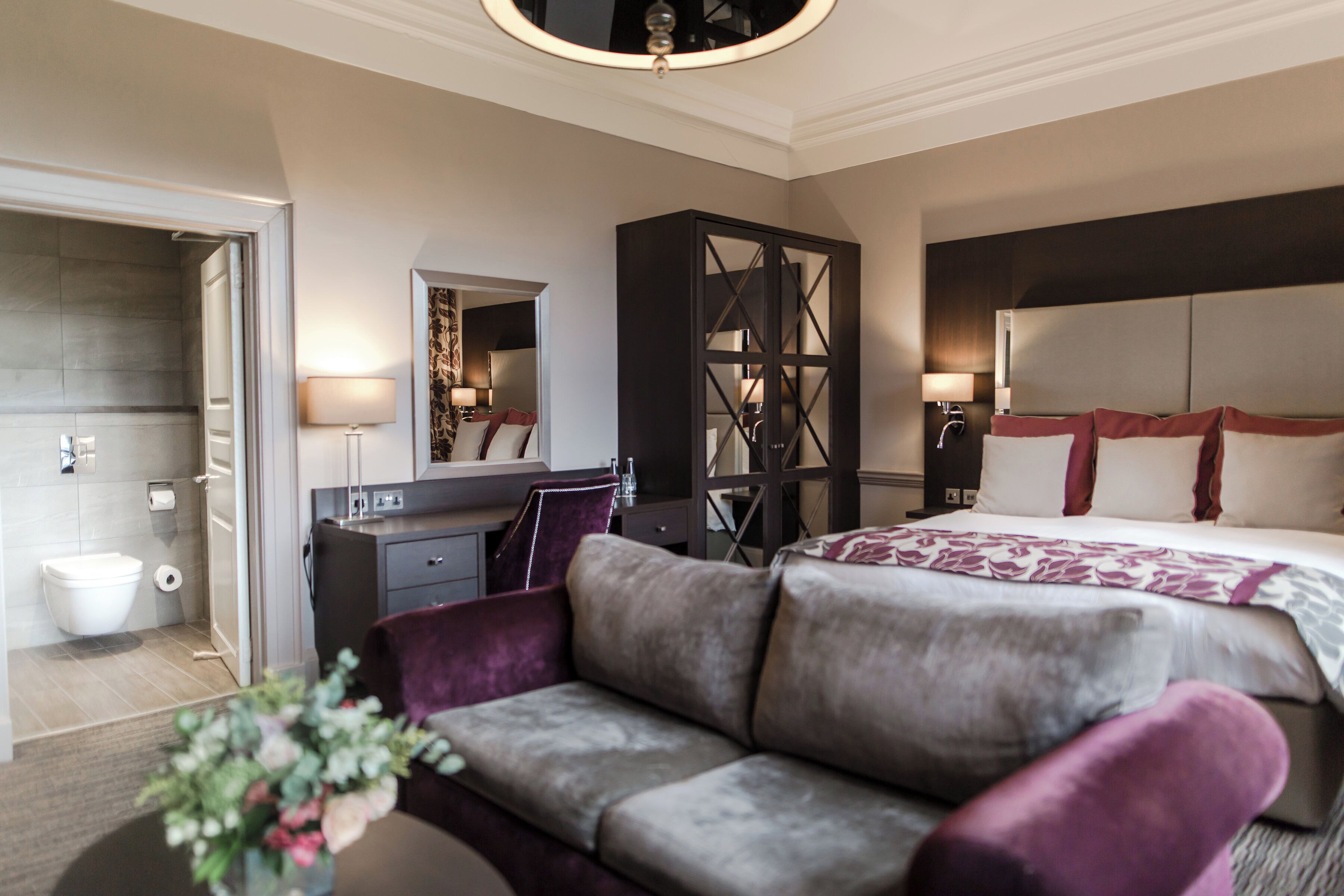 A hotel room with a bed, a sofa, a desk, a mirror, and a wardrobe.