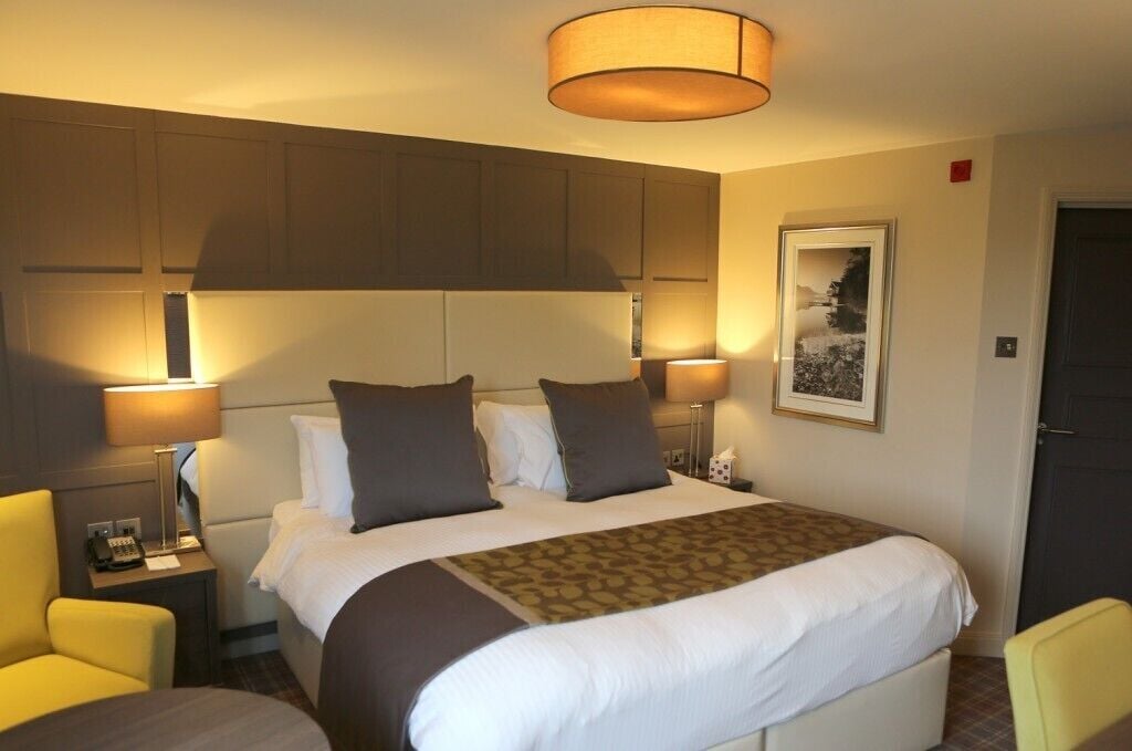 Une chambre d’hôtel avec un grand lit, deux tables de chevet avec des lampes, une chaise et un tableau encadré au mur.