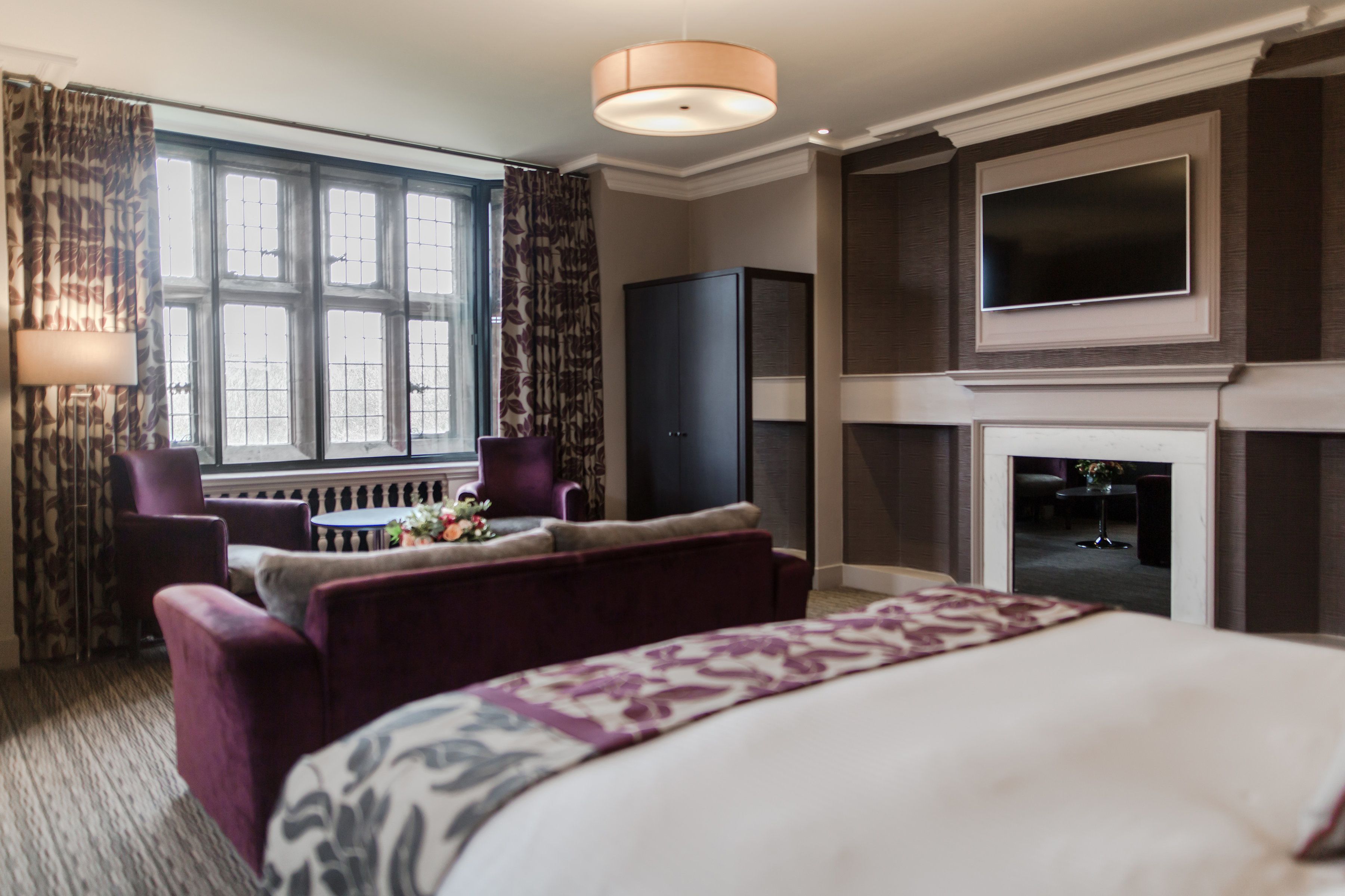 A hotel room with a large bed, a TV, a fireplace, and a seating area with a table and chairs.