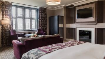A hotel room with a large bed, a TV, a fireplace, and a seating area with a table and chairs.