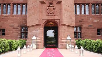 Un bâtiment en briques rouges, doté d’une entrée centrale, flanqué de fenêtres disposées de manière symétrique et surmonté d’un blason au-dessus de la porte.