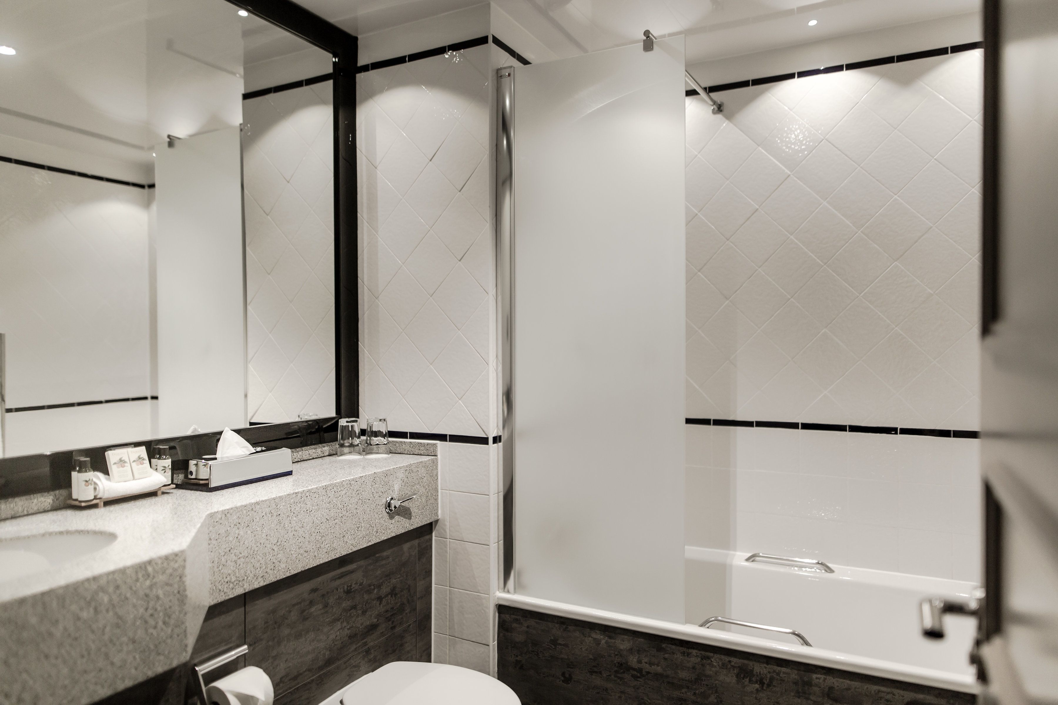 A modern bathroom with a glass-enclosed shower, a granite countertop, and a large mirror.