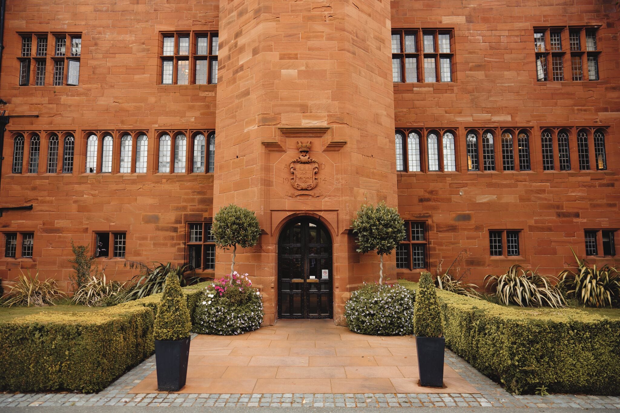A red-brick building with a central entrance, arched doorway, and a coat of arms above the door.