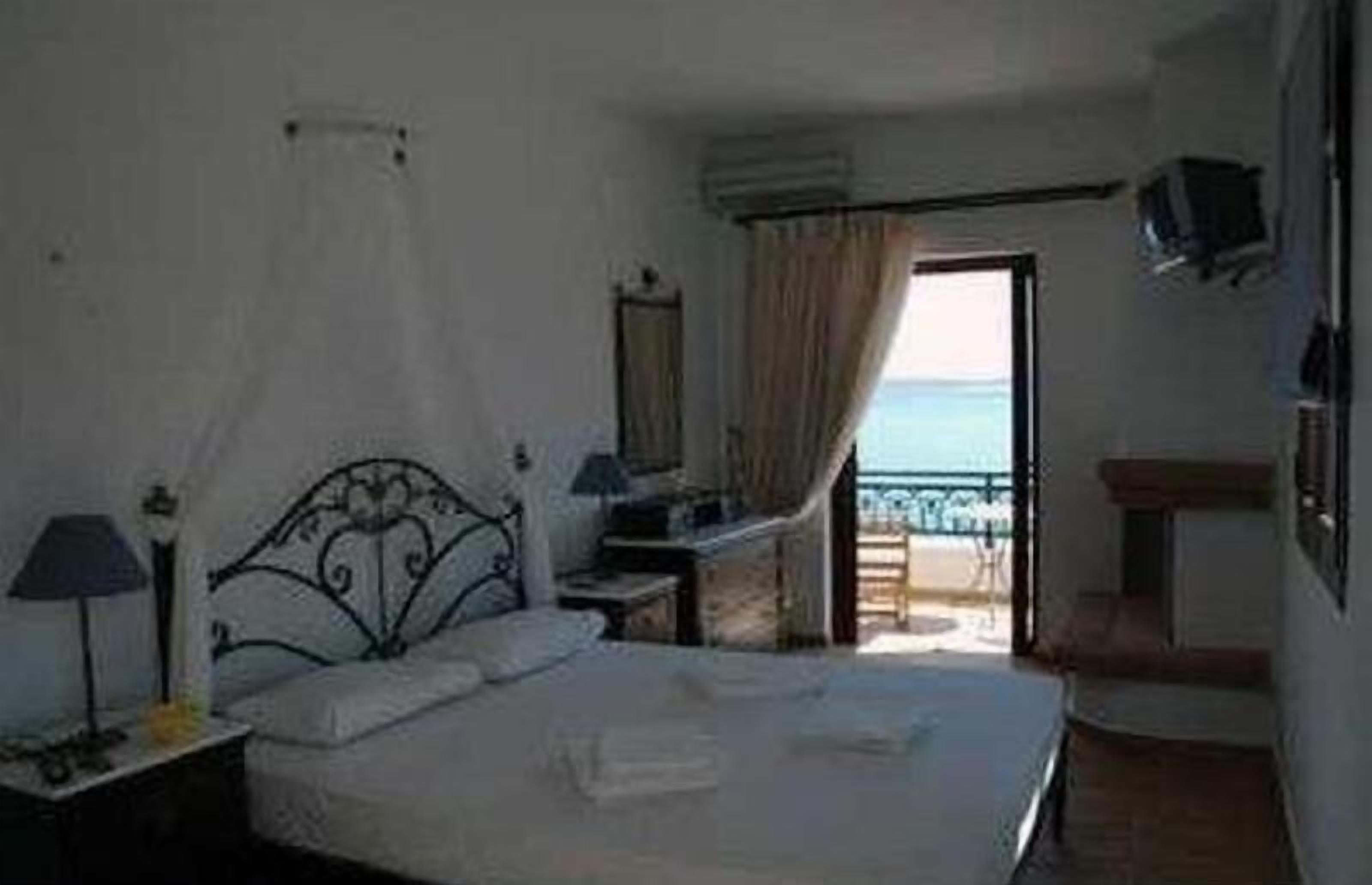 A bedroom with a bed, a nightstand, a lamp, a TV, and a view of the sea through an open door.
