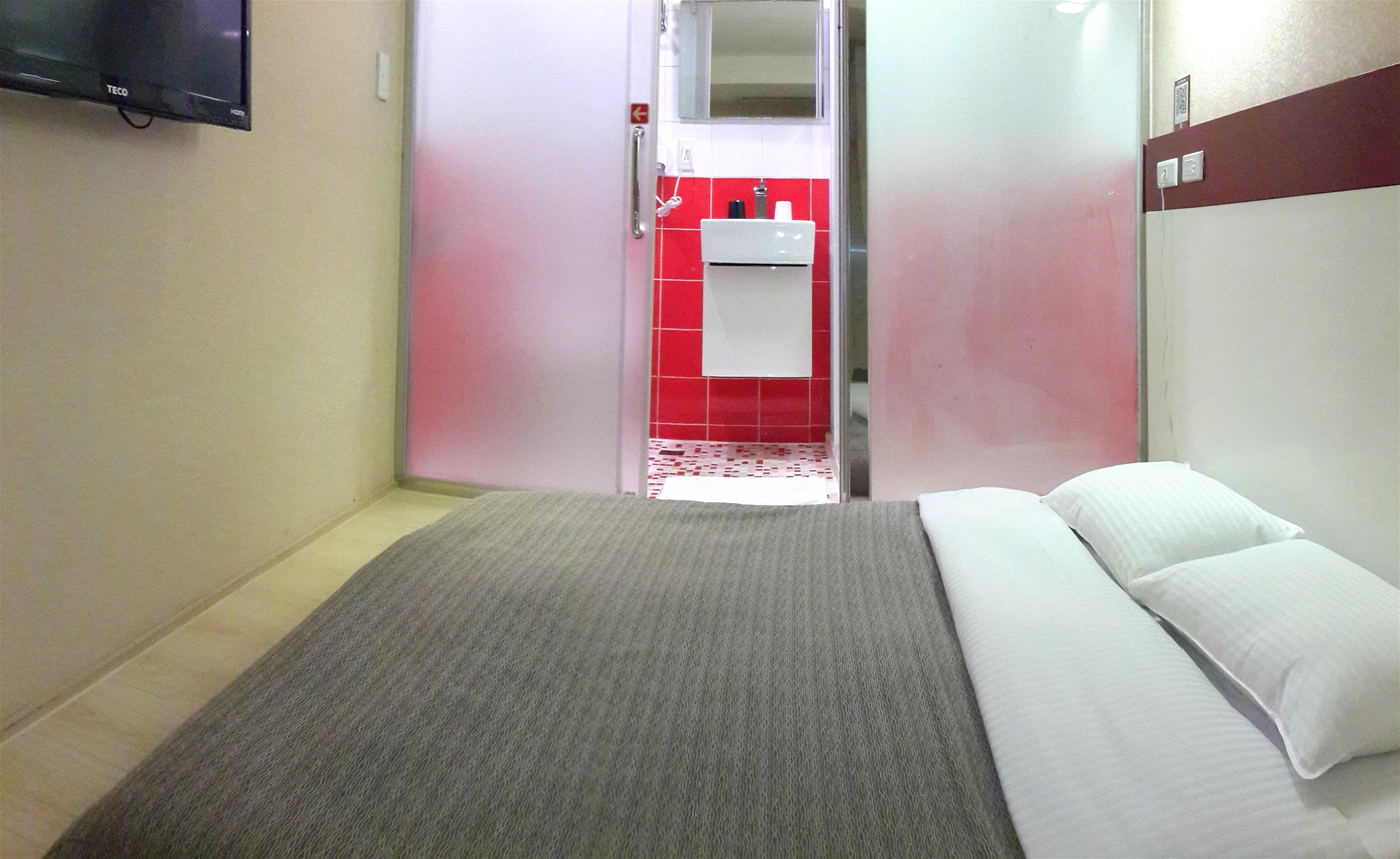 Une chambre d’hôtel avec un lit, une télévision et une salle de bain carrelée de carreaux rouges, ainsi qu’un lavabo blanc.