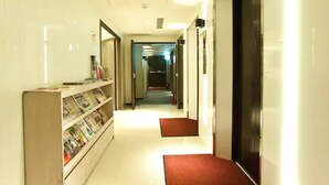 A hotel hallway with a reception desk, a bookshelf, and a door at the end. - E House Hotel (Taipei)