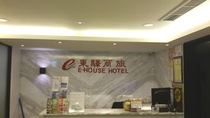 A reception desk with a marble wall, a sign reading "E-HOUSE HOTEL", and various informational brochures and a small display of items. - E House Hotel (Taipei)