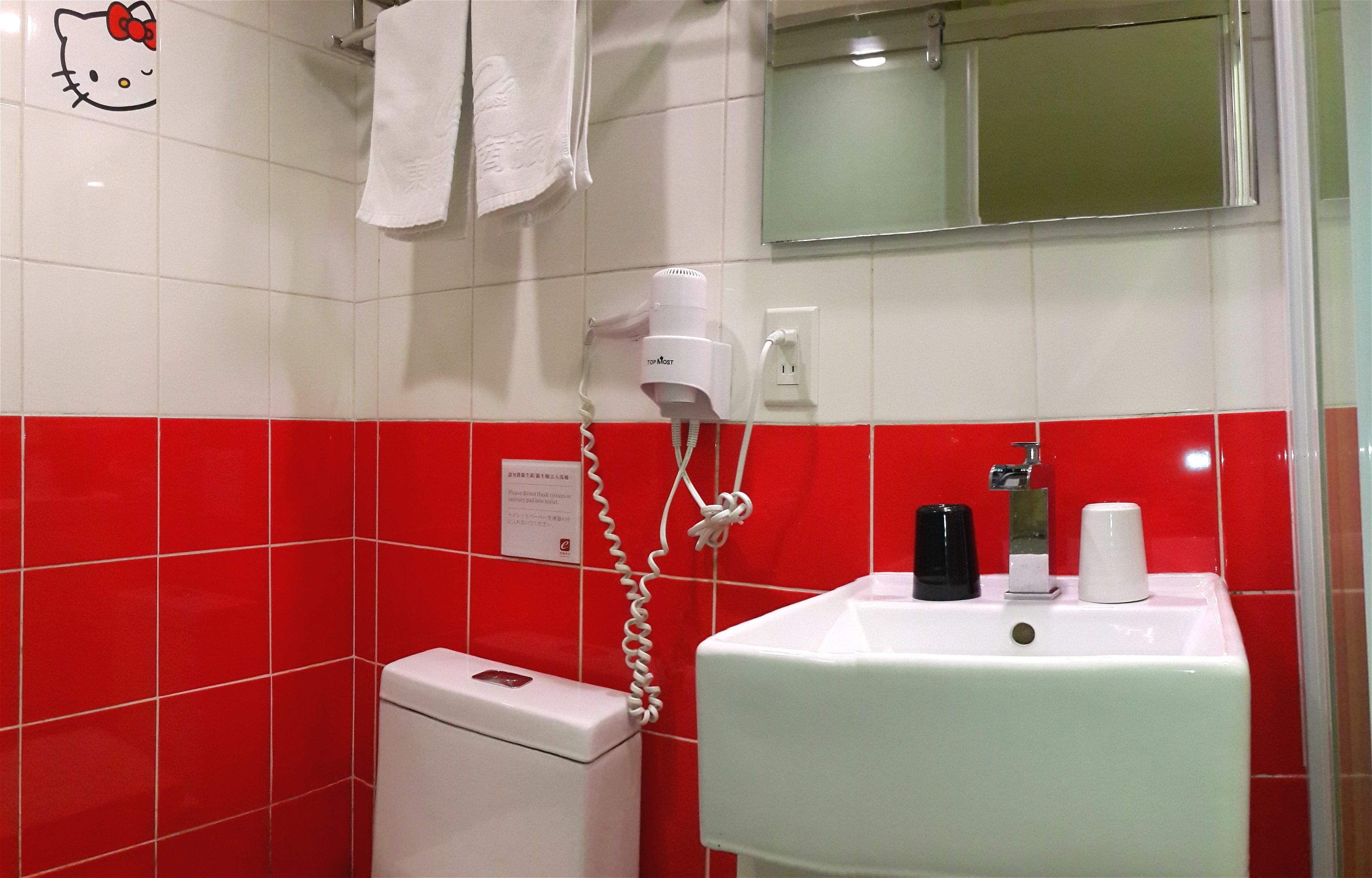 A bathroom with red and white tiles, a white sink with a mirror, a hairdryer, and a toilet.