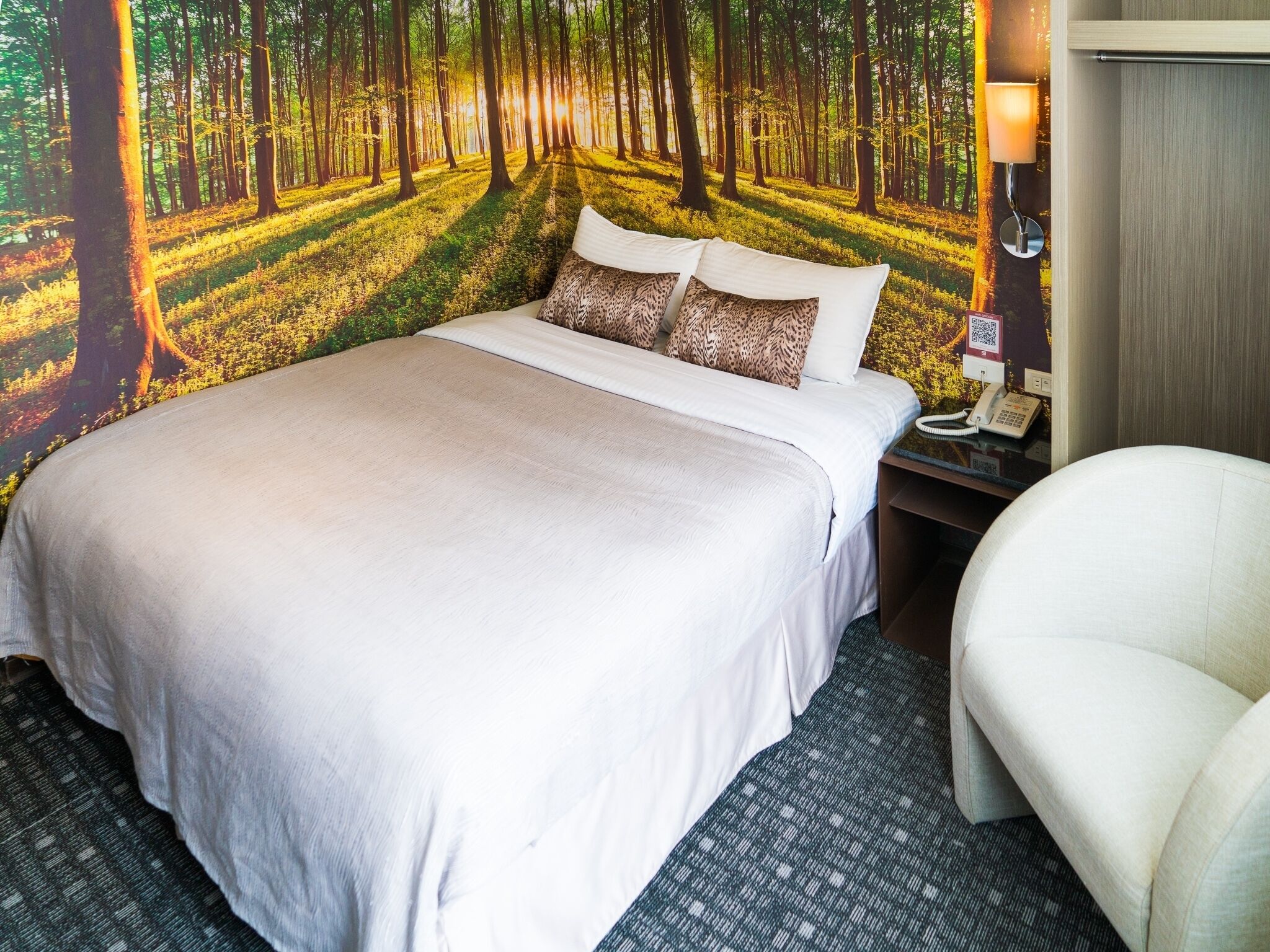 A hotel room with a large bed, a nightstand with a lamp, and a chair.